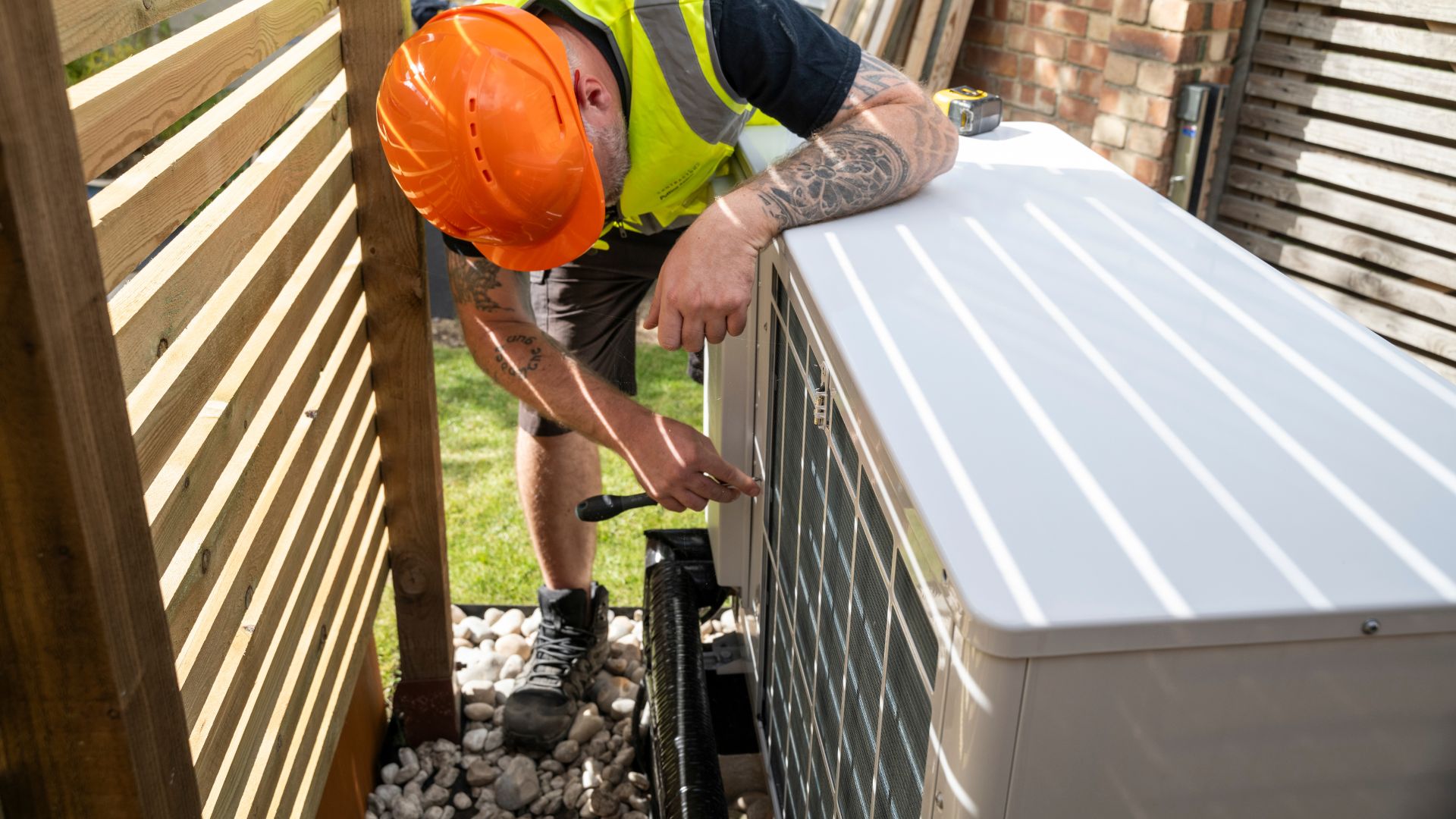 Technician in safety gear inspecting outdoor HVAC unit next to wooden fence