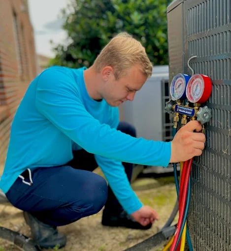 Technician checking pressure gauges on HVAC system outside building
