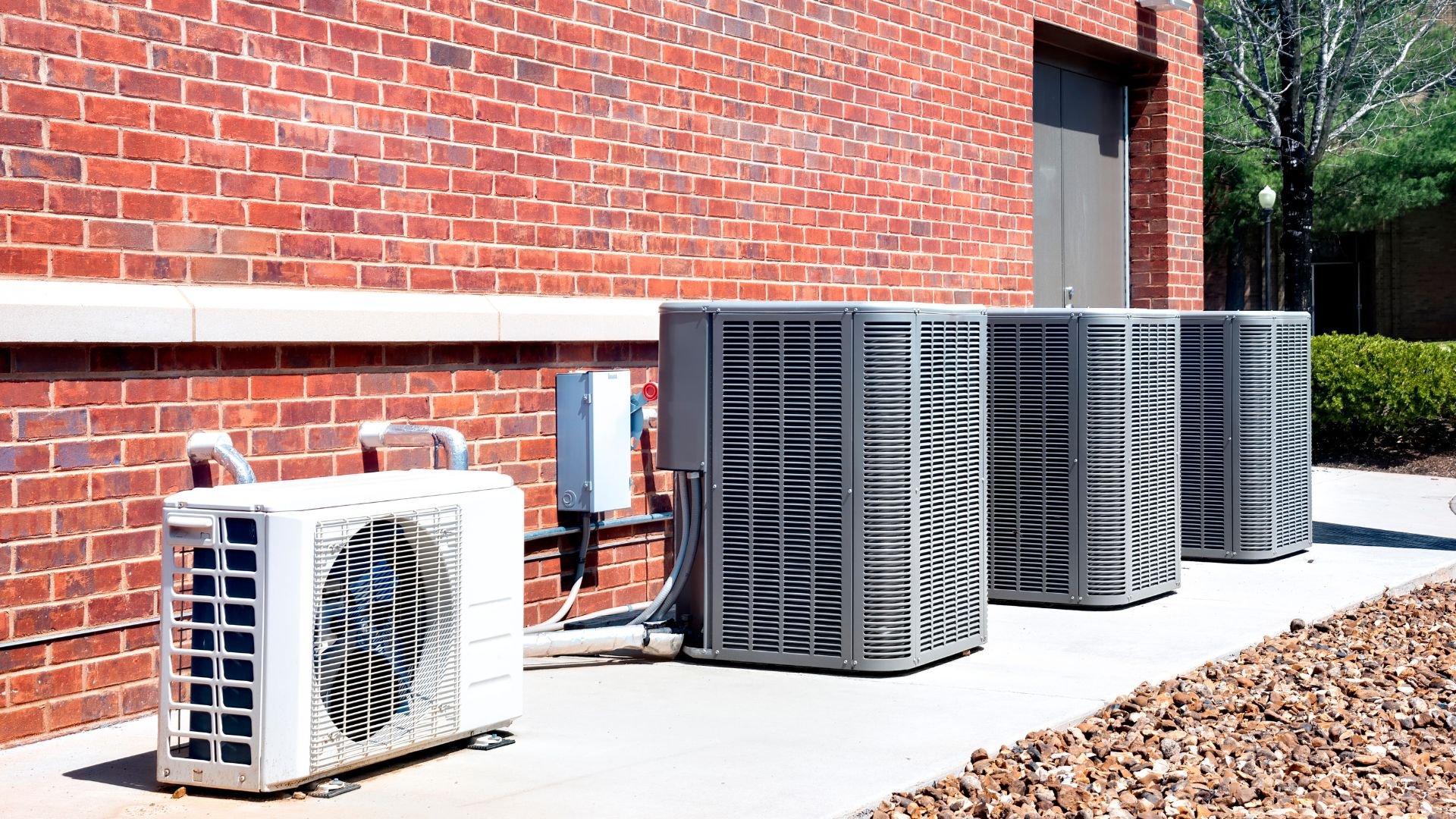 Multiple air conditioning units lined up against a red brick building