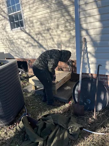 Person working with wood near air conditioning unit and house exterior