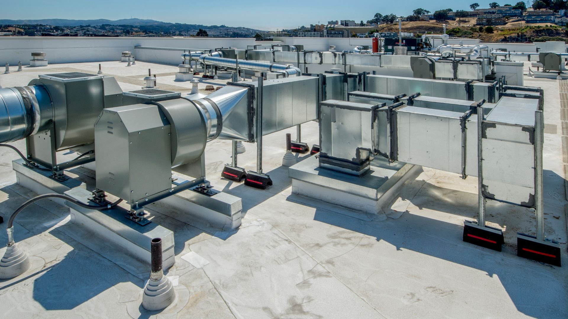 Industrial HVAC units on a white rooftop with hills in background